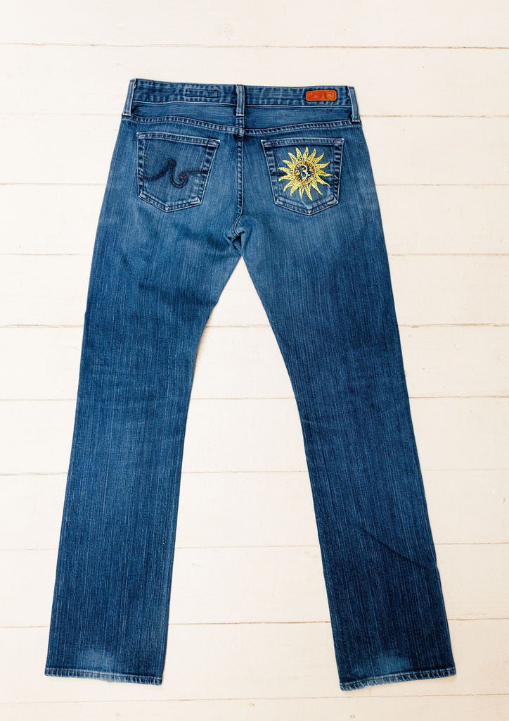 These jeans are hand-embroidered by a group of talented makers in Guatemala using traditional techniques. The front of the jeans features a colorful embroidery with the words "Hello There" 